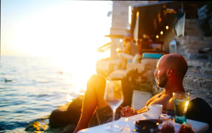 A young man relaxes at an outdoor café by the Croatian seaside, enjoying the sunset while sipping an espresso in the evening light.