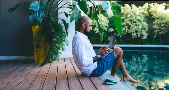 A remote worker types on a laptop beside a pool in Bali, Indonesia.