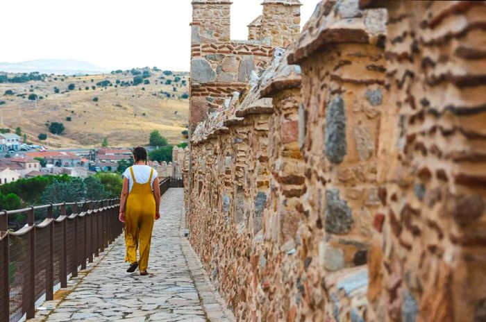 A young woman in dungarees strolls along the medieval city walls of Ávila