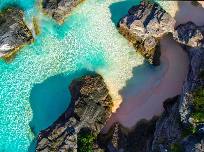 An aerial view showcasing rock formations with patches of pink coral sand beyond Bermuda's Horseshoe Bay.