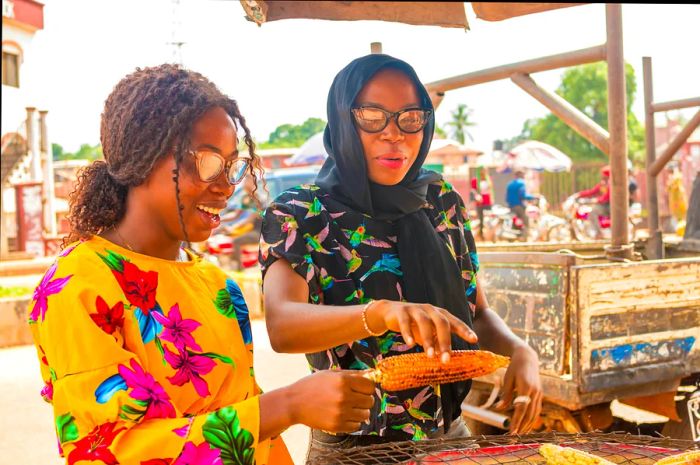 Two young women enjoying roasted corn from a street vendor in Nigeria