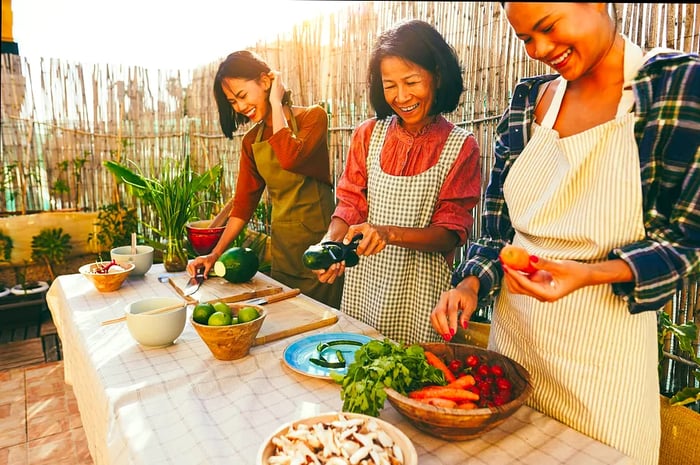 Three individuals collaborate to prepare food at a long communal bench