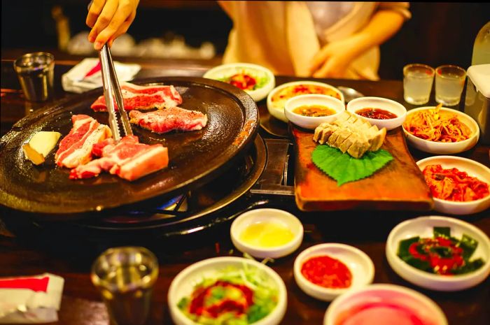 Enjoying the renowned Korean Barbecue featuring thick cuts of pork belly alongside an array of side dishes on Jeju Island