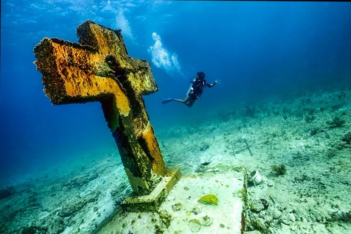 A scuba diver glides past a cross statue on the ocean floor at Cruz de la Bahia, Isla Mujeres, Caribbean Sea.