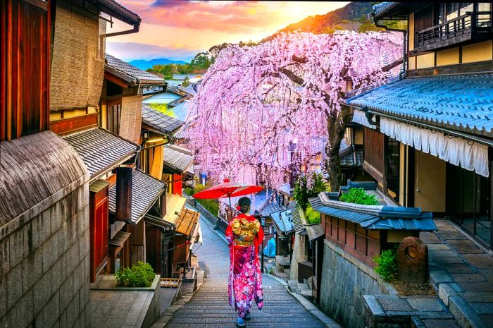 A woman dressed in traditional Japanese attire carries a decorative umbrella as she strolls between historic wooden buildings.