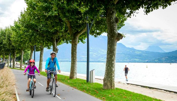 A parent and child cycle side by side on a scenic lakeside path