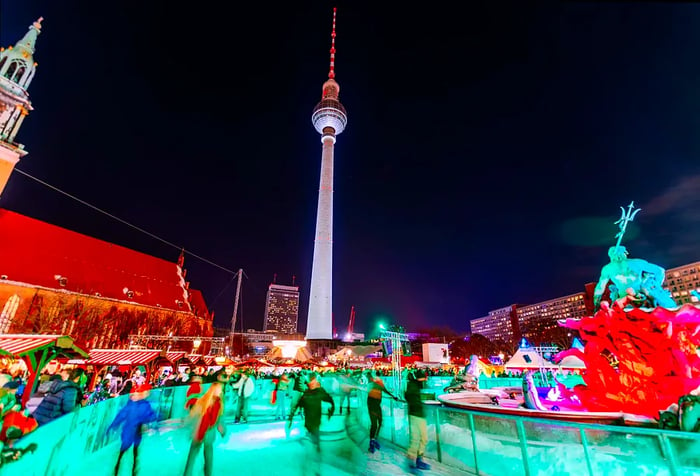 Ice skaters enjoy the festive atmosphere at the Rotes Rathaus Christmas Market, with the Berlin TV Tower visible behind them.