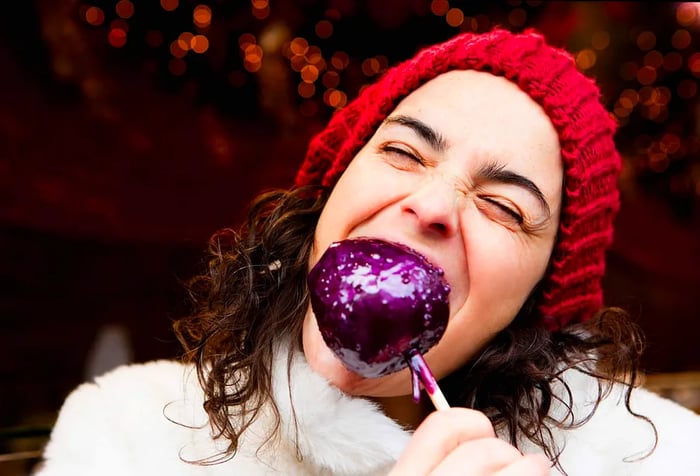 A woman enjoying a bite of a candied apple.