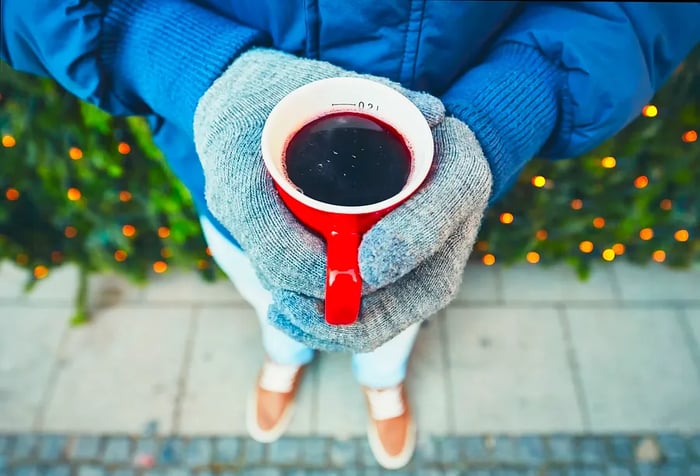 A man in a jacket and gloves holds a cup filled with a red beverage.