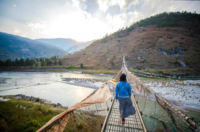 A teenager strolls across a long suspension bridge spanning a river.