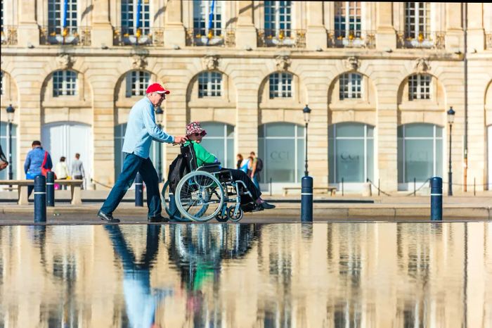 A man assists a woman in a wheelchair outside Place de la Bourse, Bordeaux, Aquitaine, France