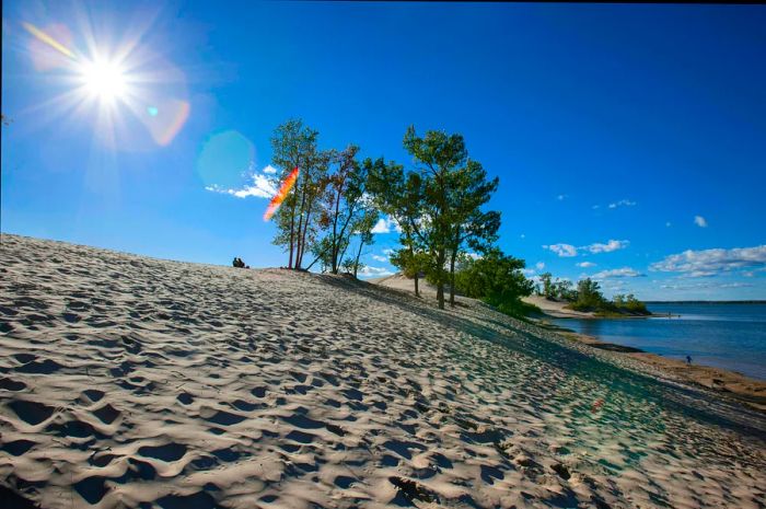 Two individuals relax atop a sand dune, gazing down towards a serene lake.