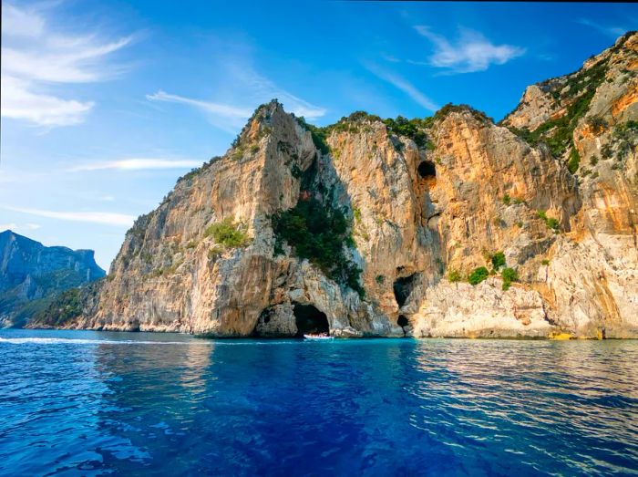 A rugged limestone cliff towers above the crystal-clear blue sea.