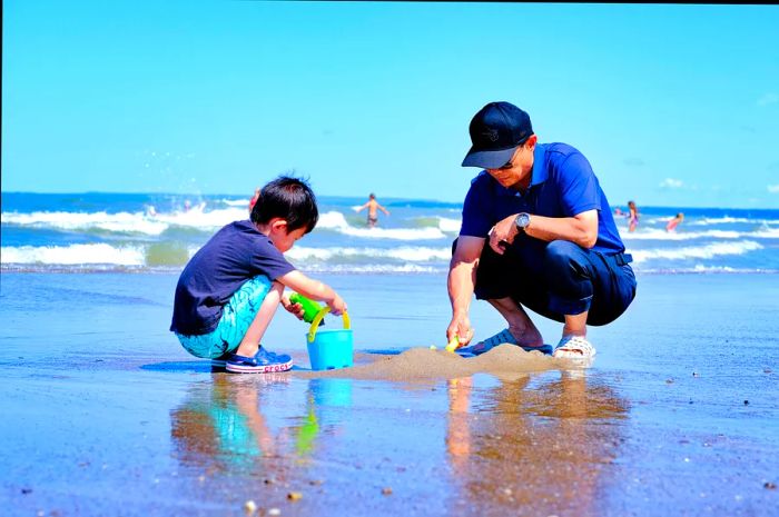 A grandfather enjoys playing on a sandy beach with his grandson