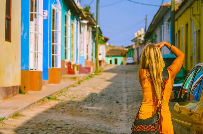 A young girl with blonde hair captures the charm of a street in Trinidad, her vibrant yellow dress standing out against the old, quiet street that attracts both tourists and locals.