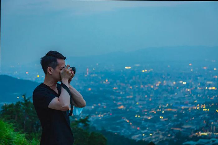 An Asian man captures photographs from the summit of Mt. Daimonji in Kyoto, Japan.