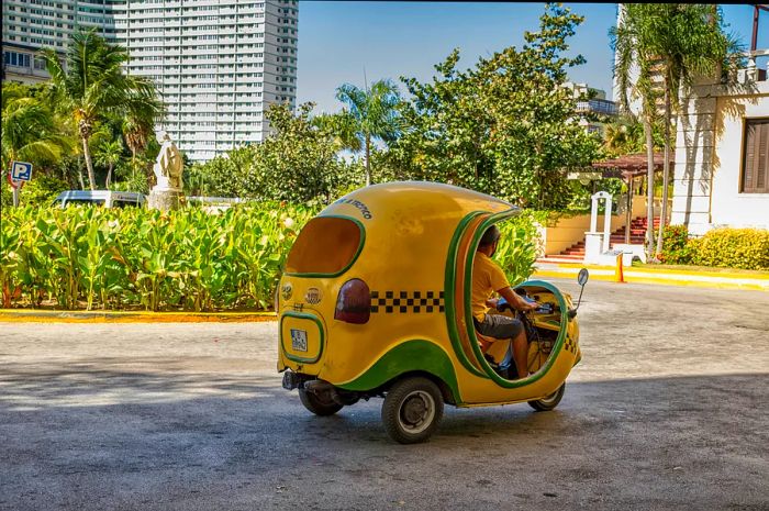 A yellow, coconut-shaped Cuban motorbike taxi, known as a Coco taxi, located near the Hotel Nacional de Cuba in Havana