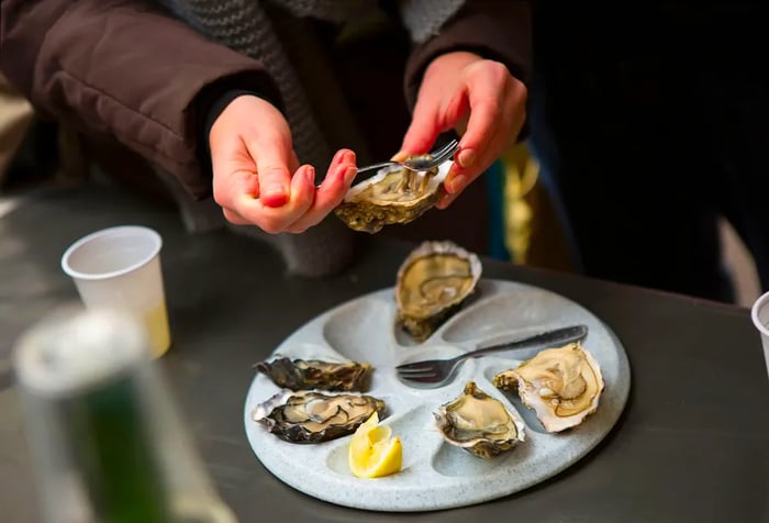 A person using a fork to delicately extract an oyster from its half-shell.