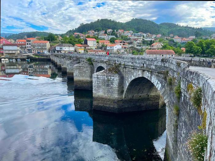 A Roman bridge crosses a tranquil river in Arcade, Spain, along the Camino de Santiago.