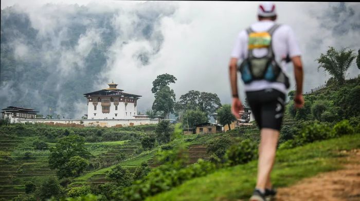 A hiker with a backpack traverses a trail beside a monastery in Bhutan