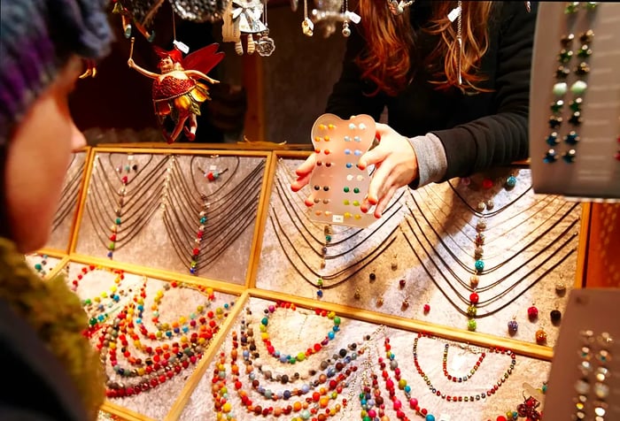 Hands showcase a variety of jewelry earrings in a shop filled with vibrant necklaces.