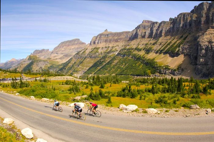 Three cyclists zoom past rocky mountains in Glacier National Park, Montana.