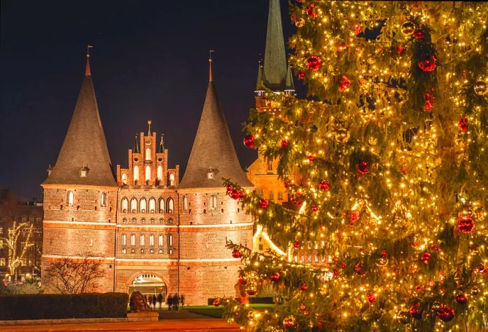 The illuminated Holstentor gate at night, complemented by a radiant Christmas tree in the foreground.