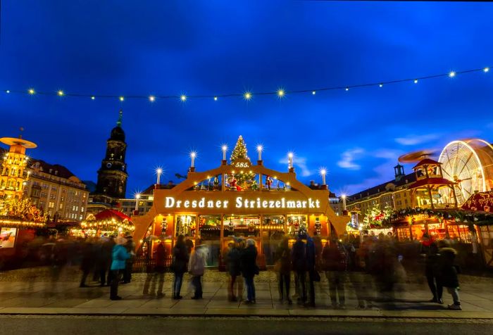 A radiant golden arch marks the entrance to a Christmas market set in a square surrounded by tall buildings in Dresden.