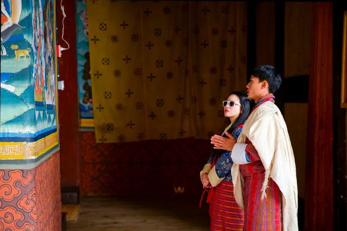 A young female traveler and a local guide admiring a mural on a wall in Paro, Bhutan