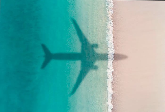 The shadow of an airplane glides over a beach with crystal-clear turquoise waters.