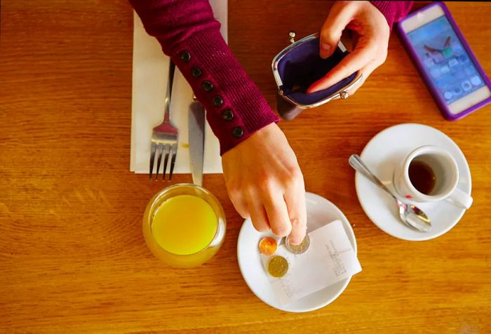 an overhead shot of a woman's hands making a payment for her juice and coffee at a table