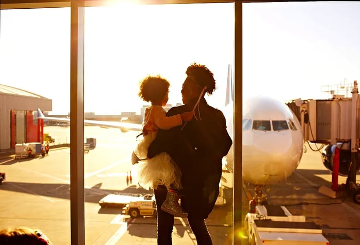 A mother and her daughter gaze at an airplane from inside the terminal.