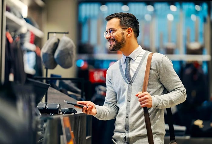 A male customer completing an online payment at the counter of a clothing store.