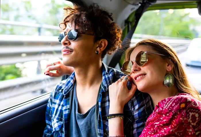 A cheerful young couple wearing sunglasses enjoys a ride in an Uber cab.