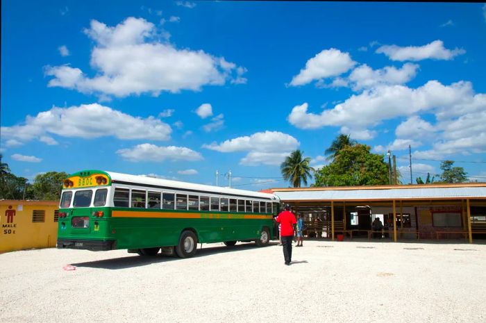 A vintage green school bus from the 1950s sits at a bus terminal in Belize City.