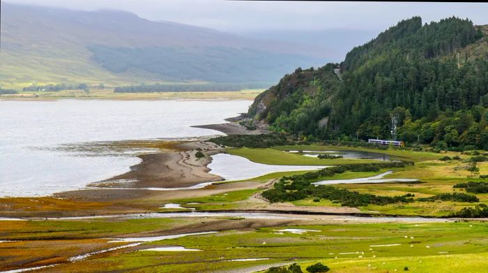 A Scotrail Class 158 diesel train makes its way over the glacial delta of the River Attadale as it follows the Kyle Line along Loch Carron, an Atlantic Ocean inlet in Scotland's West Highlands.