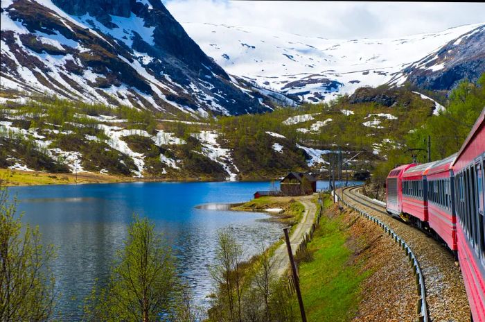 A train navigates past snow-covered peaks and a river on its route from Oslo to Bergen in Norway.