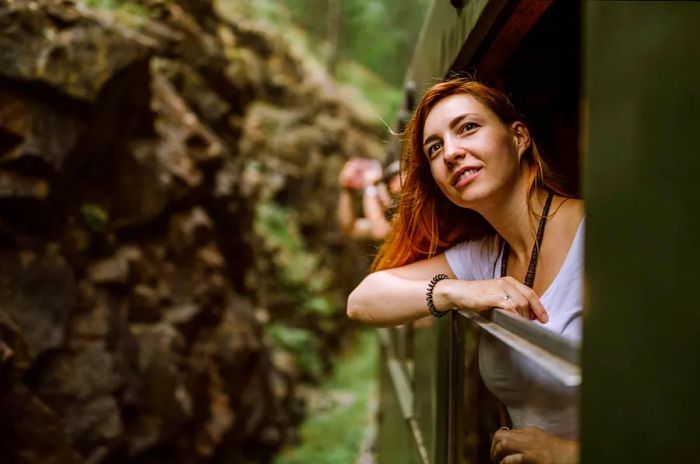 A woman enjoys her train journey, leaning out of the window to take in the beautiful scenery.