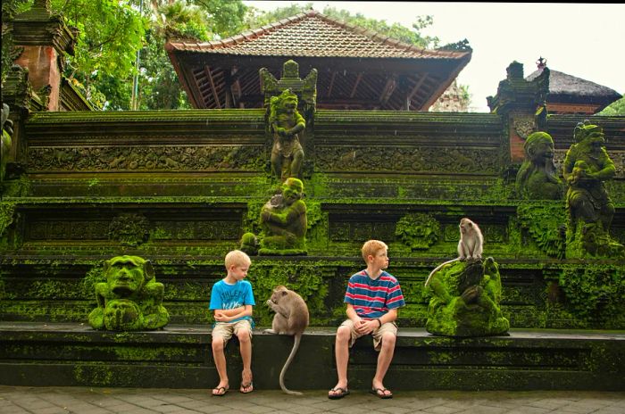 Two boys relax on a wall outside a temple, observing two monkeys