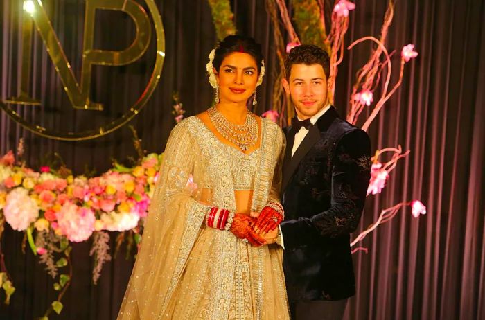 Priyanka Chopra and Nick Jonas during their wedding reception; she dazzles in an intricately beaded sari and necklace while he sports a dark velvet tuxedo.