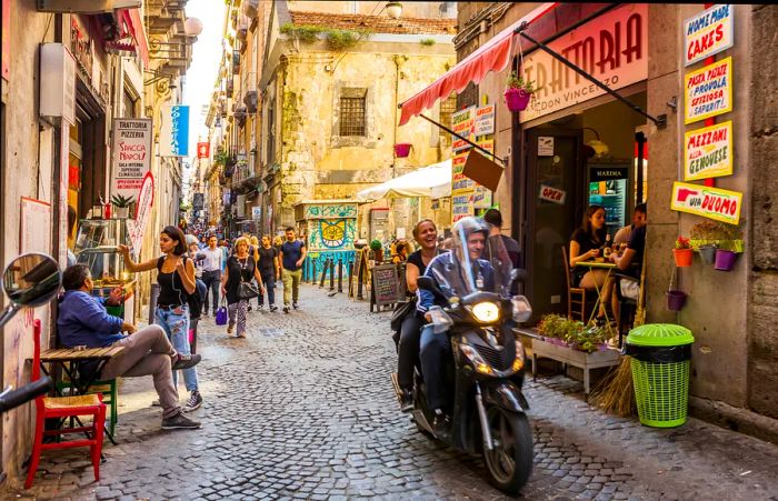 A scooter zips past shoppers on the narrow Spaccanapoli street in Naples, Campania, Italy