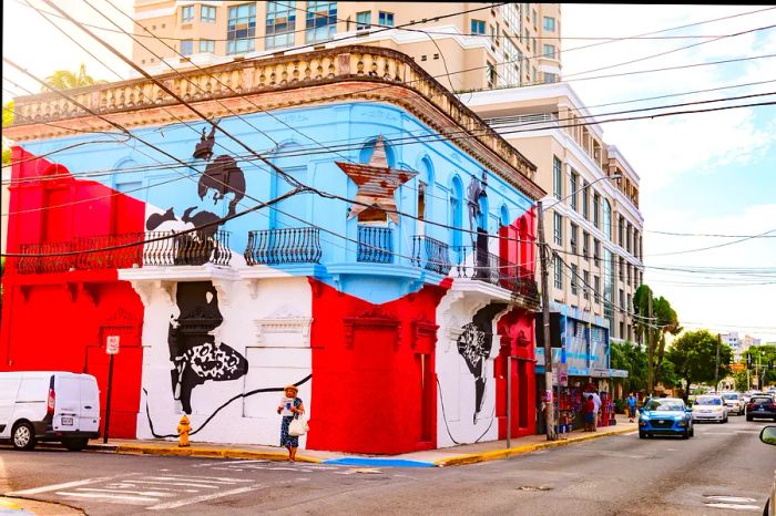 This image captures the vibrant street scene on Calle Loiza in the Santurce neighborhood of San Juan, Puerto Rico. A corner building proudly displays the Puerto Rican flag, with cars and pedestrians filling the streets and sidewalks.