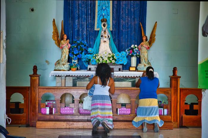 Women praying before the altar of the Black Madonna at Our Lady of Regla Church