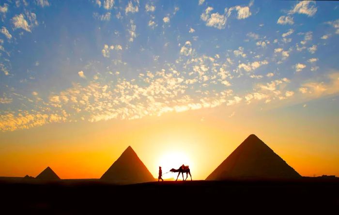 A lone tour guide riding a camel at sunset beside a massive stone pyramid in the desert.