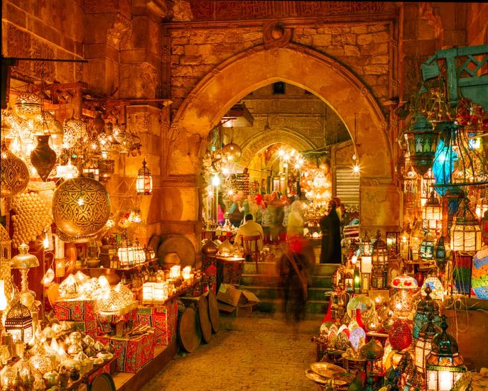 Visitors stroll through bustling alleyways illuminated by ornate lamps in a vibrant marketplace.