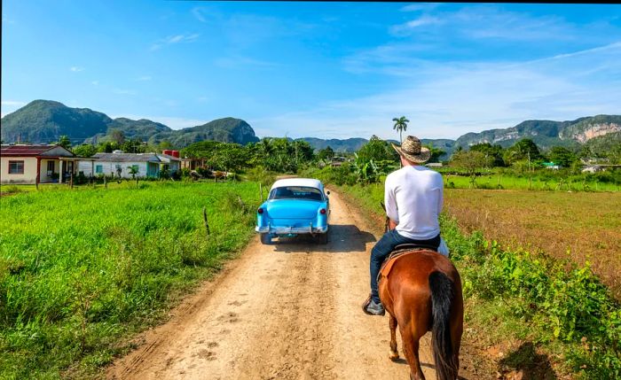 A vintage car drives past a man on horseback in Viñales, Cuba