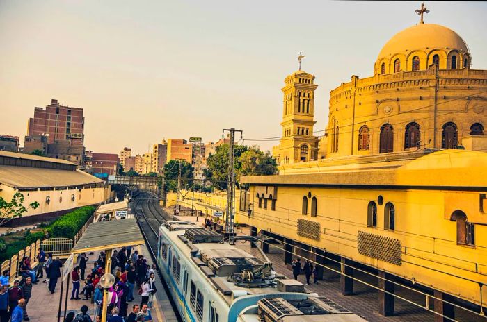 A metro train arrives at a station beside a grand church