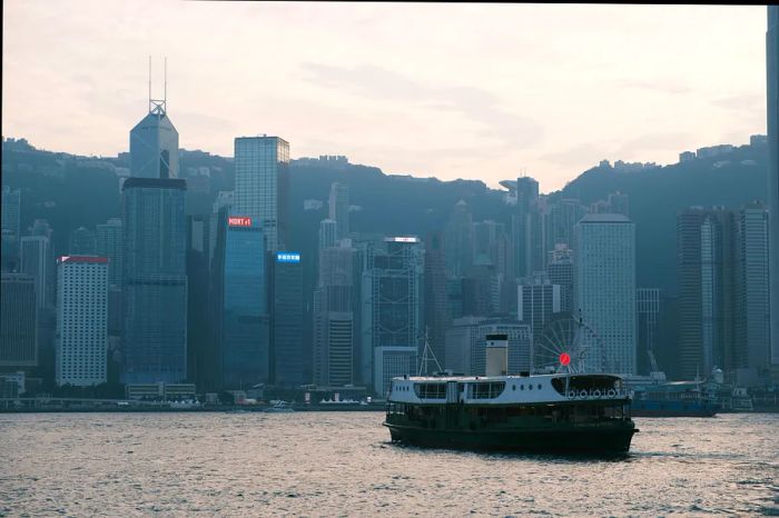 A ferry glides across a harbor with a city skyline in the background.