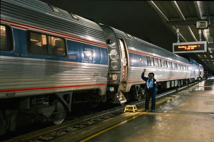 An attendant raises their arms as the Silver Meteor arrives in Savannah, emerging from the darkness of early evening.