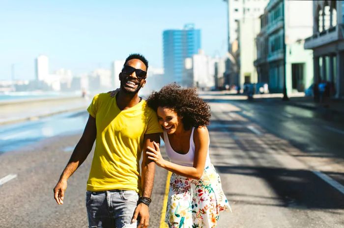 A joyful Cuban couple strolls through the sunny streets of Havana, sharing laughter.